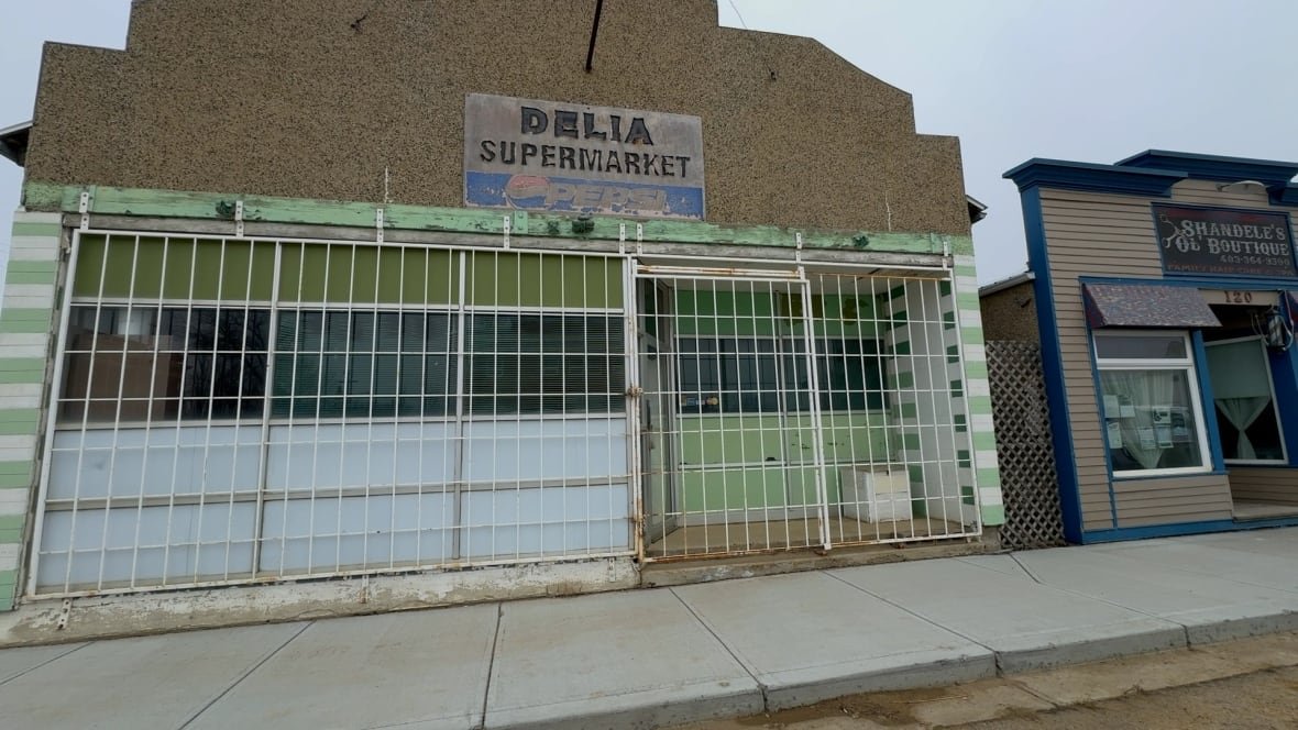 An old building that used to house the supermarket in Delia is pictured. The paint on the sign that reads Delia Supermarket is peeling. Metal bars cover the door and windows.