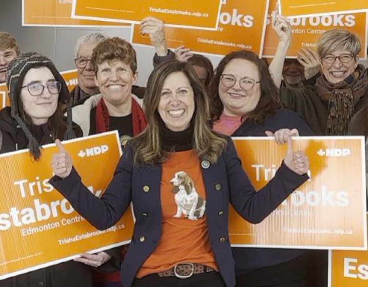 a woman with supporters holding orange signs behind her.