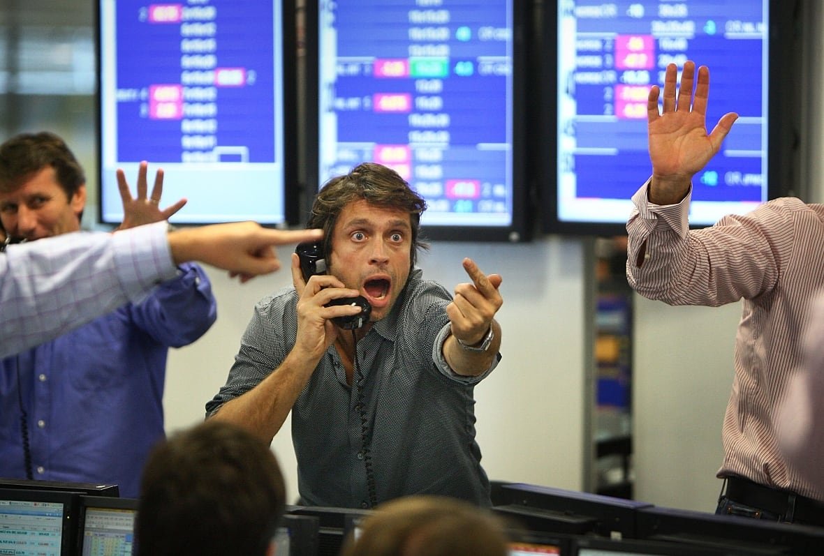 A panicked-looking stock broker gestures dramatically while talking on a phone. 