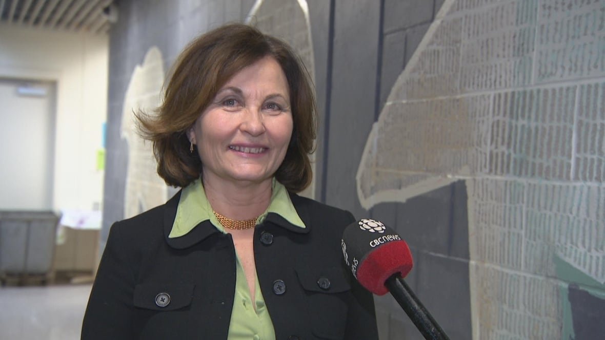 Dominique Griffon wears a green blouse and black blazer as she stands in front of the new mural in the Polar Bear Lounge at the AVC