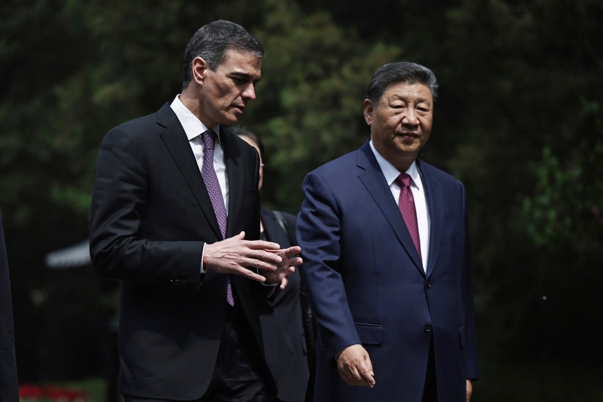 Two cleanshaven men in suits are shown walking outside, one is dark haired and the other is older and Asian.
