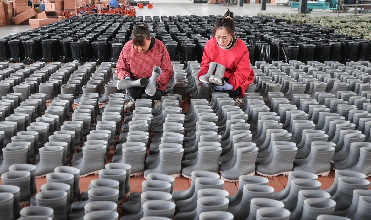 Women standing over tables filled with identical rain boots