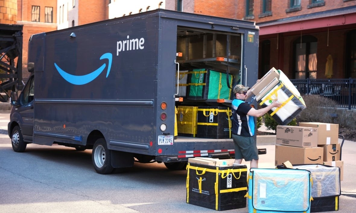 A truck is being loaded or unloaded by a man who is in the middle of hoisting a box. A number of other boxes are scattered on the ground around him. The truck says "Prime" on the side.