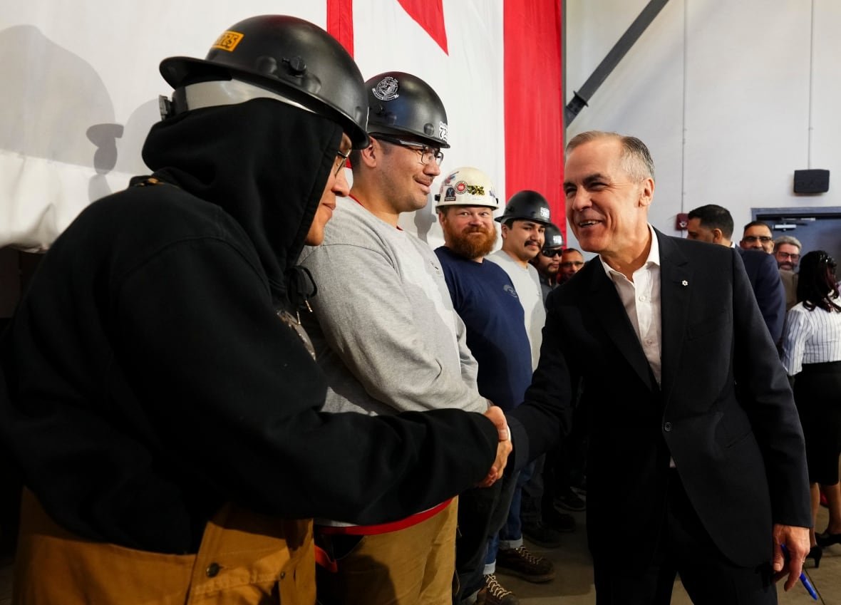 suit-clad man shakes hands with a hard-hat-clad worker while others look on.