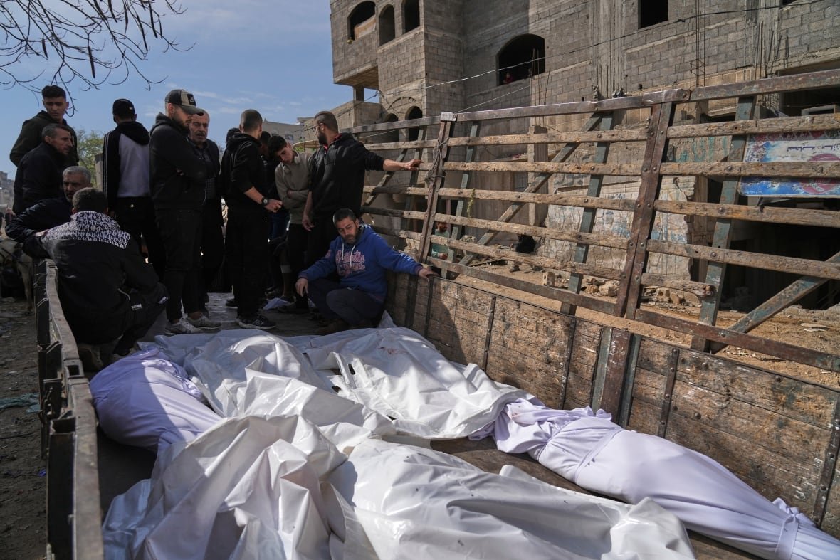 People on the back of a truck with bodies wrapped in white shroud.
