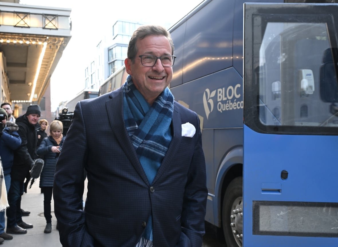 A man smiles next to a blue bus on a city street.