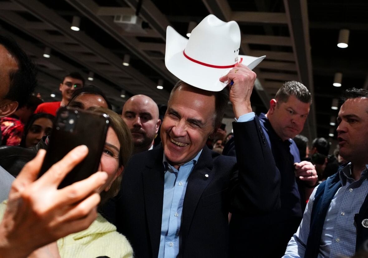 A man holds up a cowboy hat.