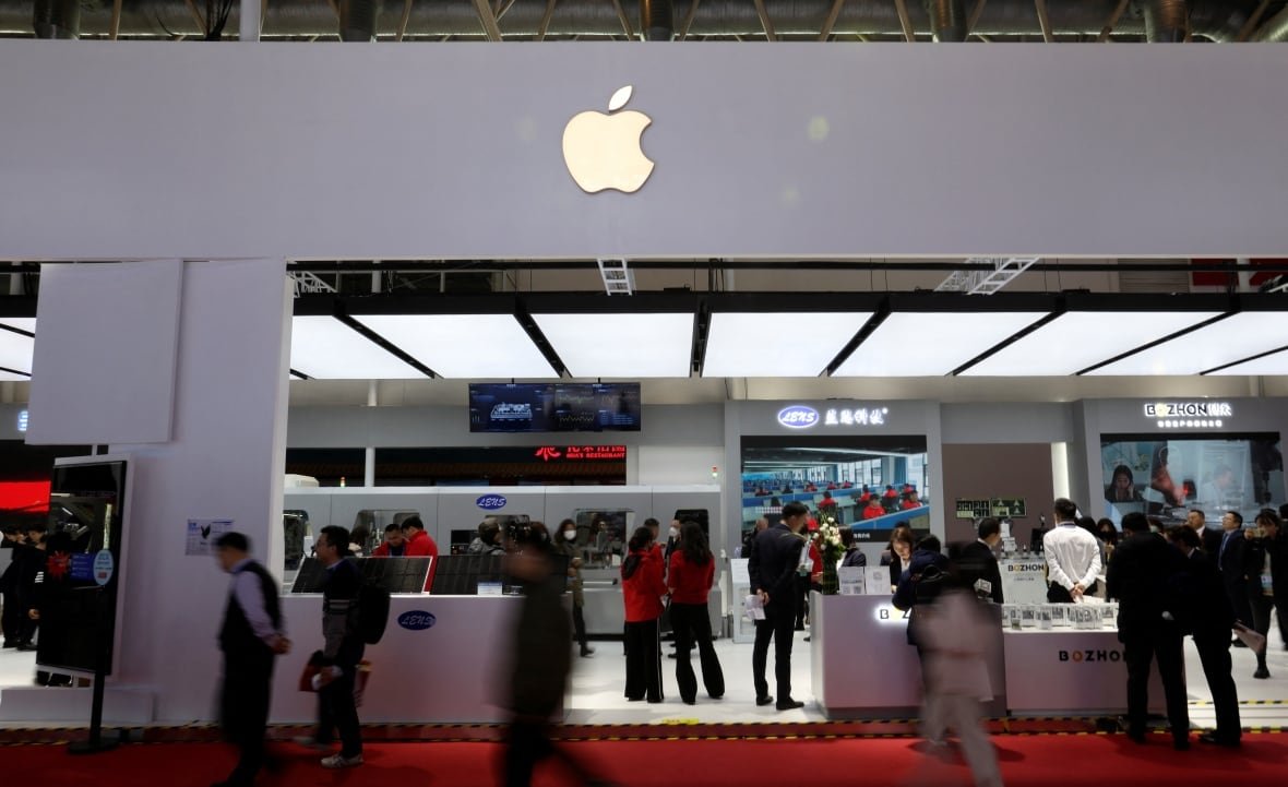 People walk in front of an Apple store in blurred silhouettes. A number of people stand inside the store. 