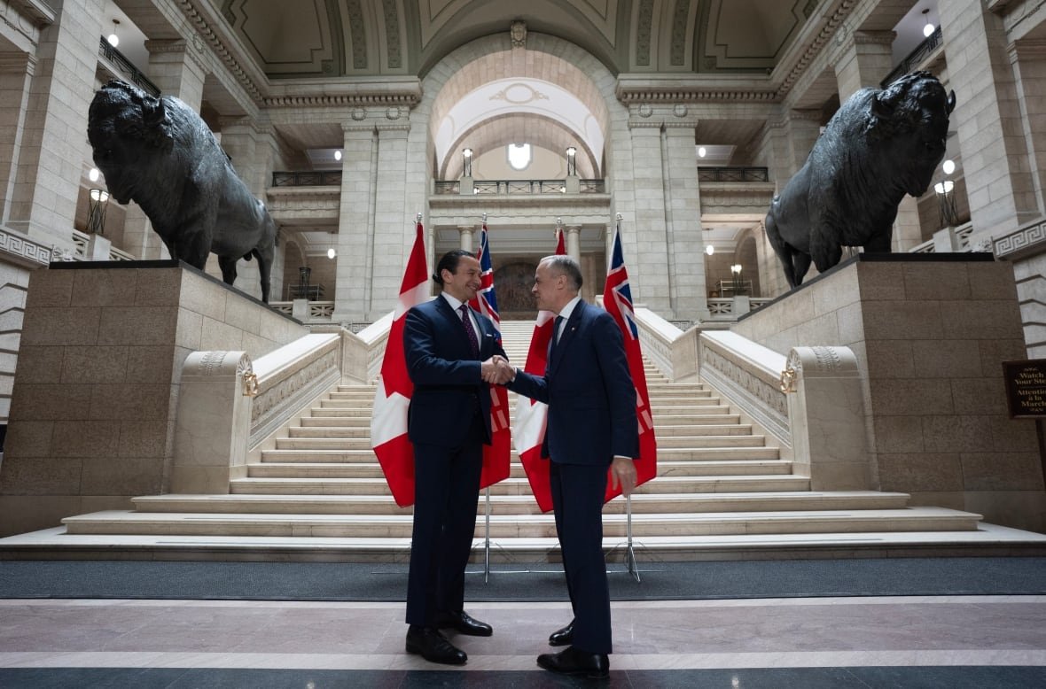 Two men shake hands in front of flags in a legislature lobby. 