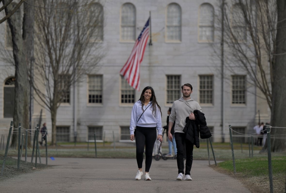 A young bearded man and a woman walk on a path at what appears to be a campus-like setting.