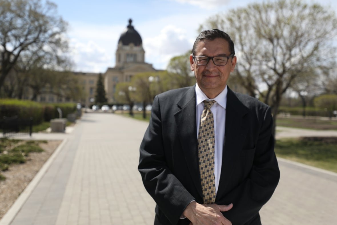 A man in a suit stands outside the Saskatchewan Legislature on a sunny day.