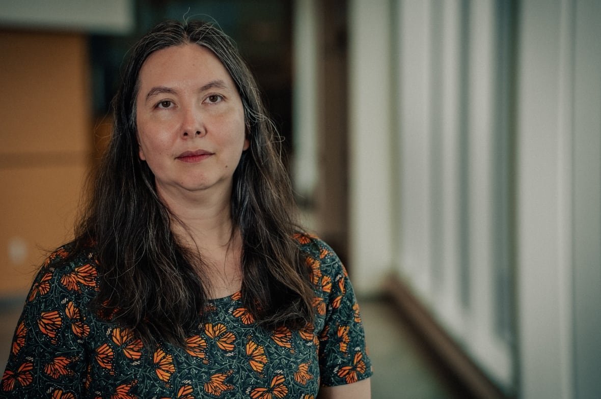 A woman with long brown hair and strands of grey wearing a green t-shirt with orange floral print. 