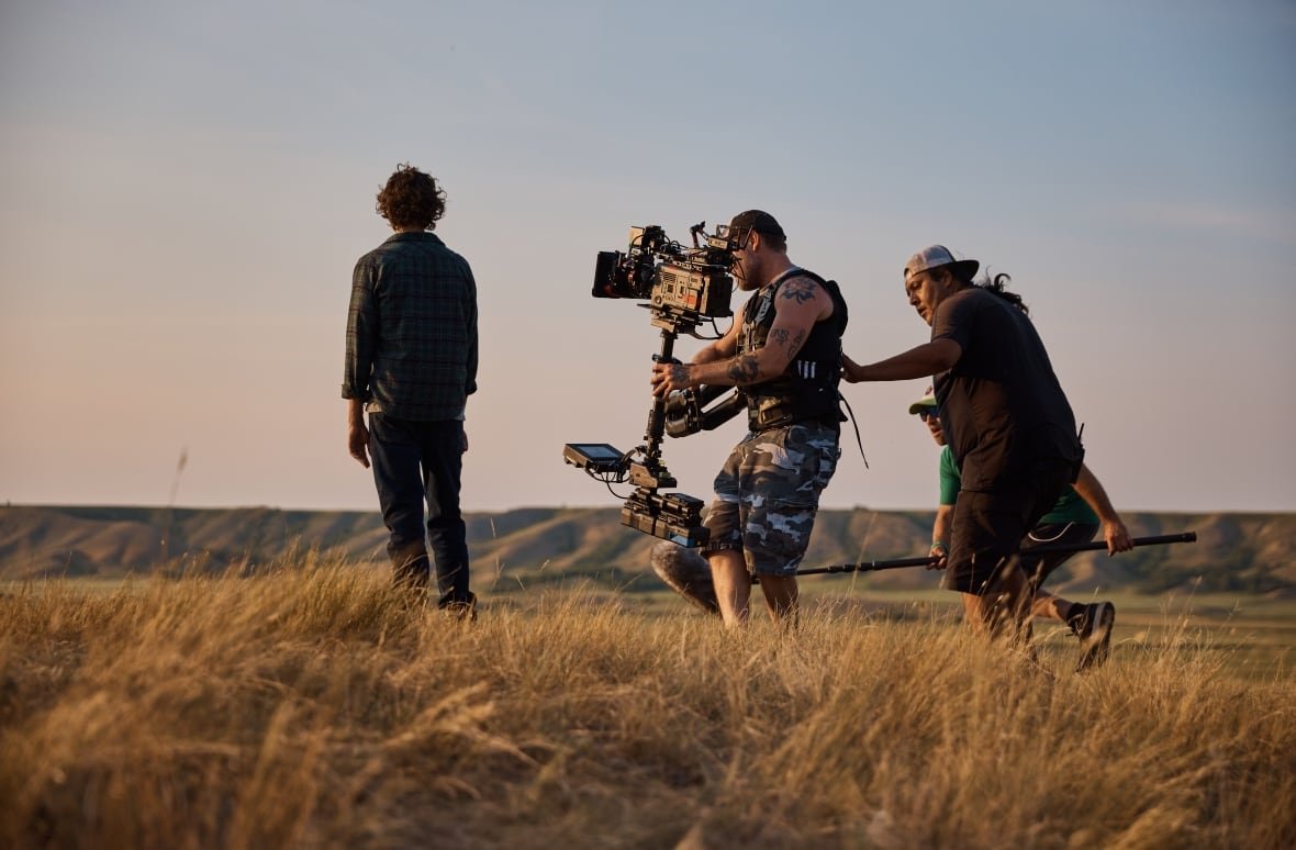 Two camera guys film a man standing atop a prairie valley.