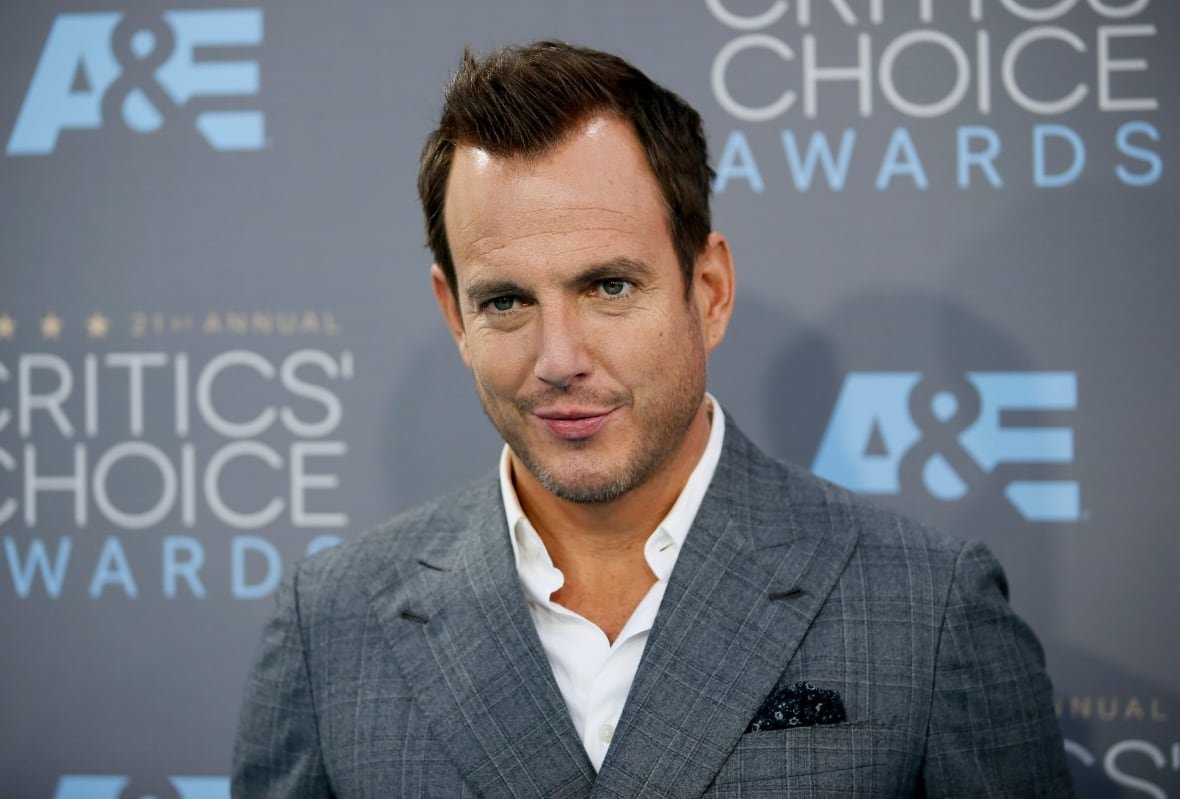 A man in a suit smirks while posing for a photo.