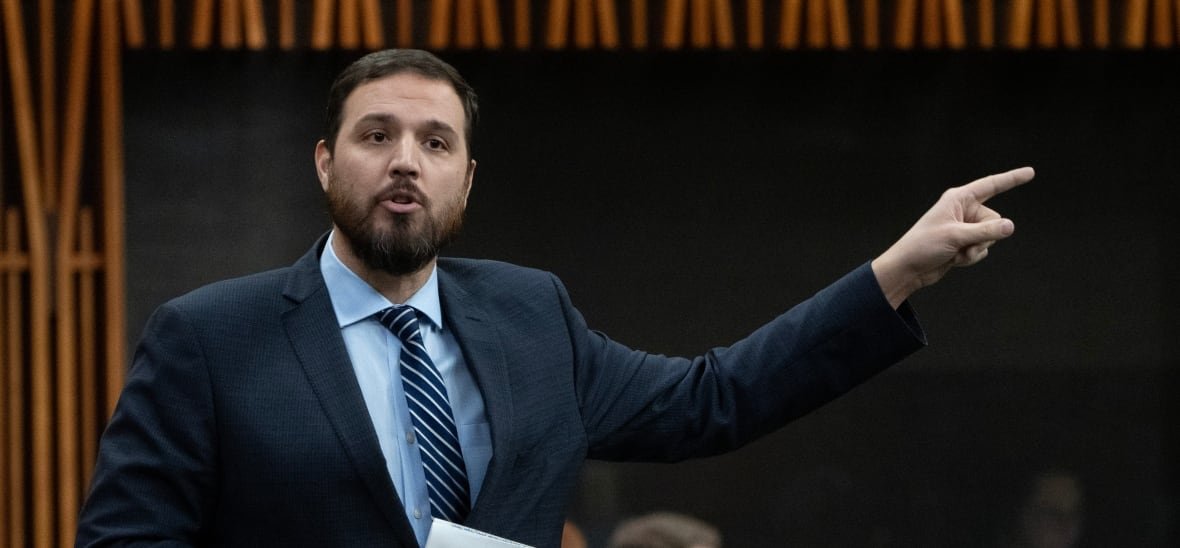 A man in a suit raises his arm while speaking.