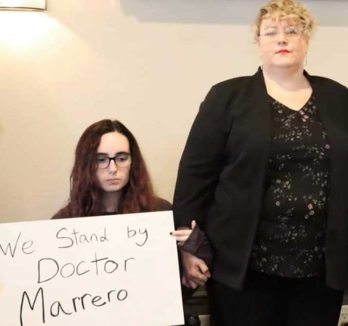 A young woman in a wheelchair holding a sign that reads, 'We stand by Doctor Marrero,' beside an older woman.