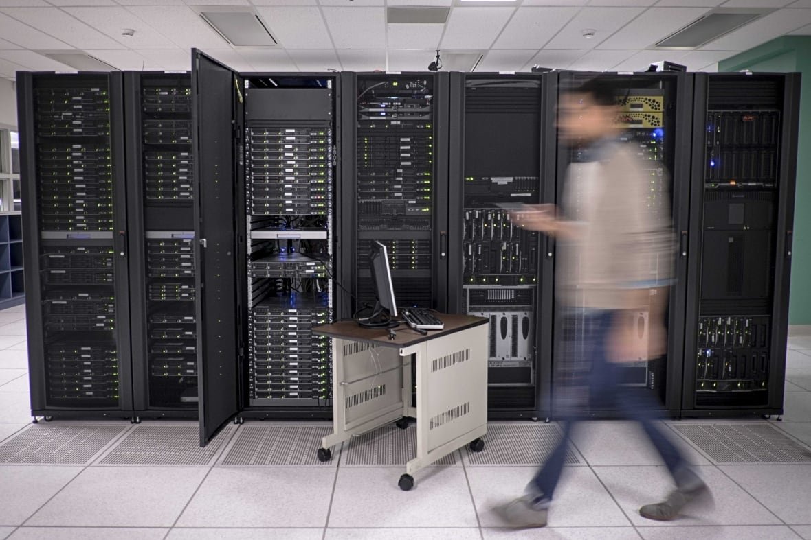 A man, blurred, walks in front of wall of servers