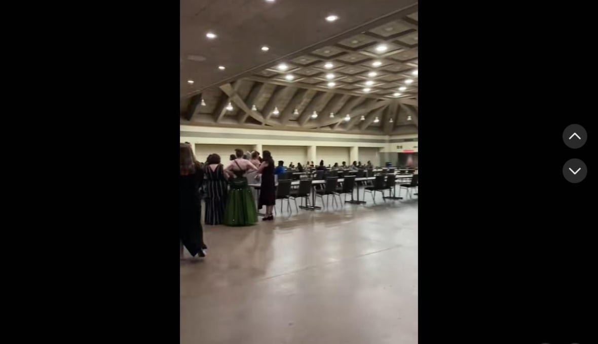 A Tiktok screenshot shows a large room that is mostly empty, with a few people in fancy dresses standing near some tables. 