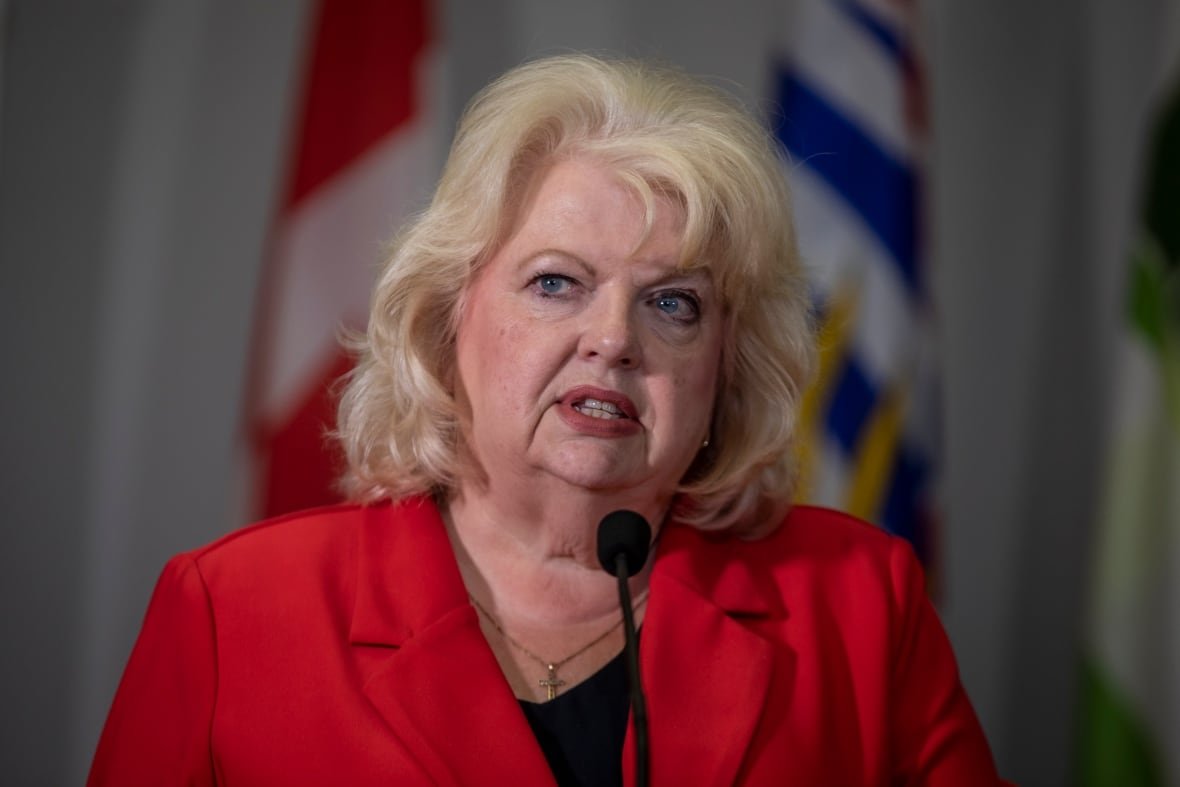 A white woman with short blond hair and a red top speaks.