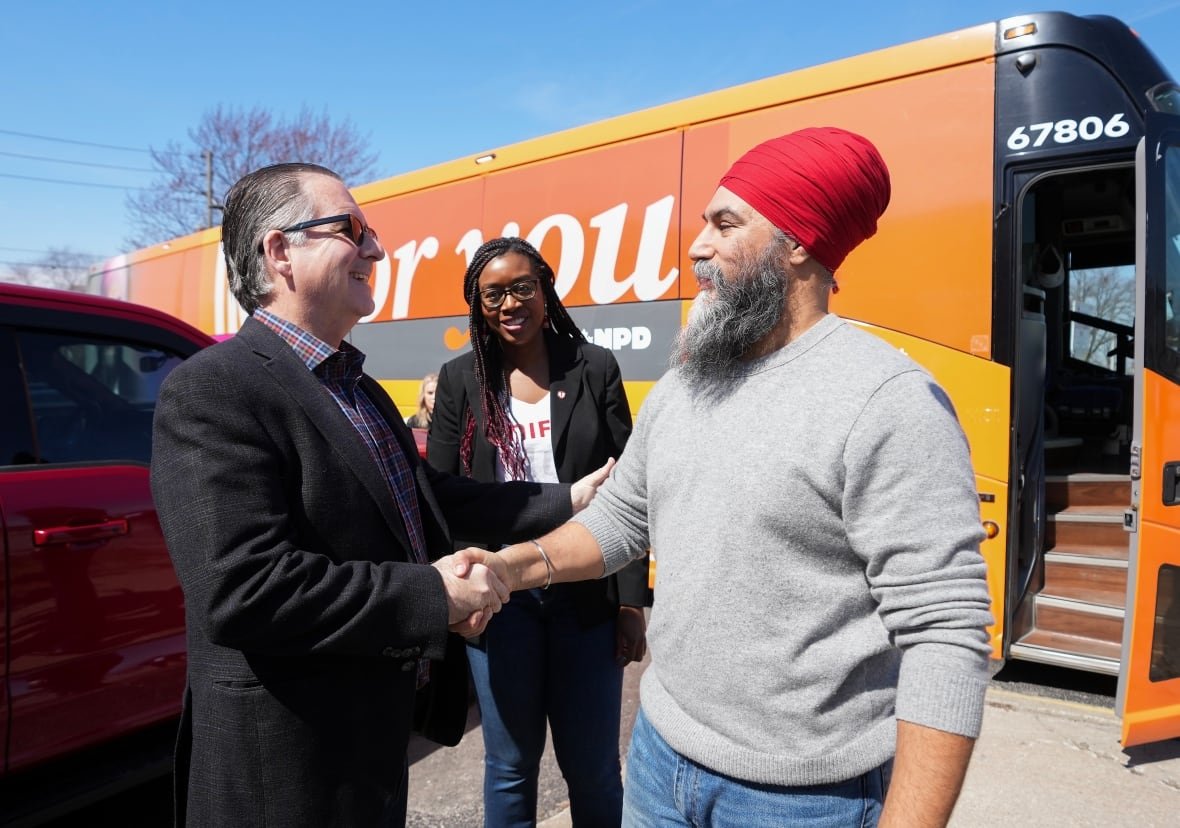 A man with thin grey hair shakes hands with a man wearing a red turban