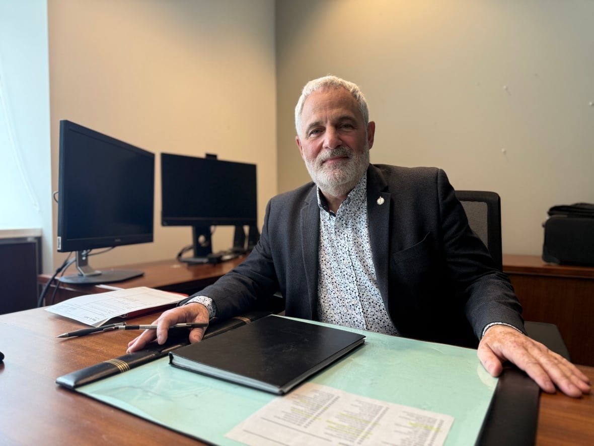 A man with thin white hair sits in a chair.