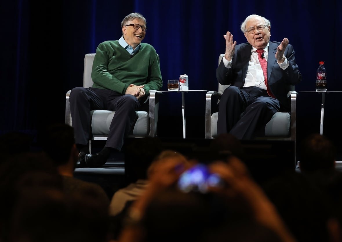 Bill Gates and Warren Buffett sit in chairs on a stage.