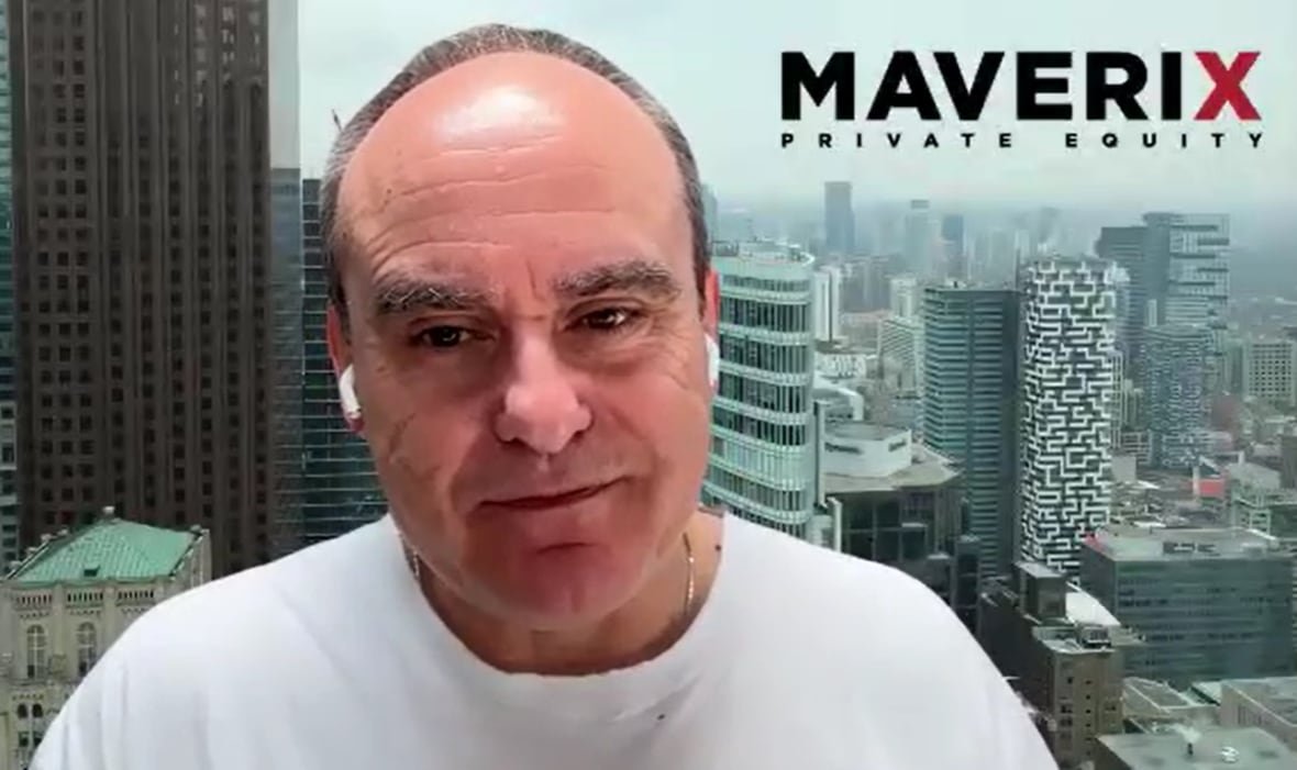 John Ruffolo sits in front of a green-screened cityscape.