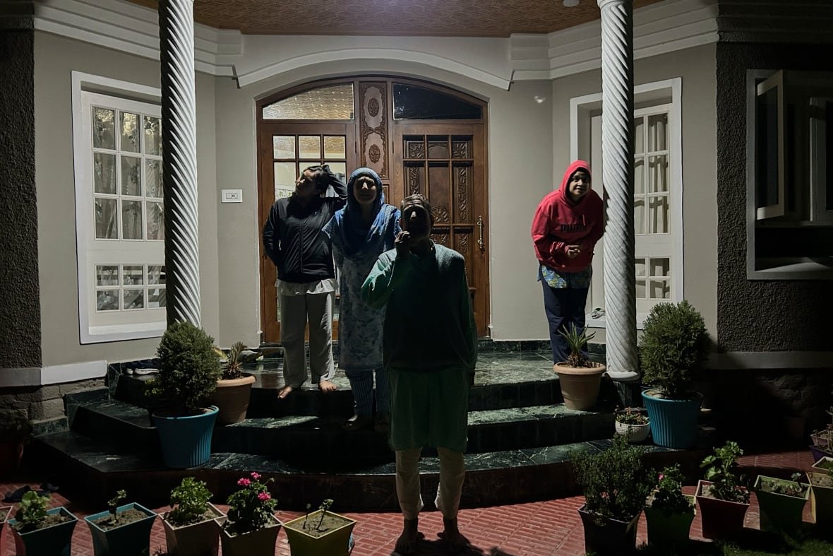 Four people watch the sky at night from a front doorstep.
