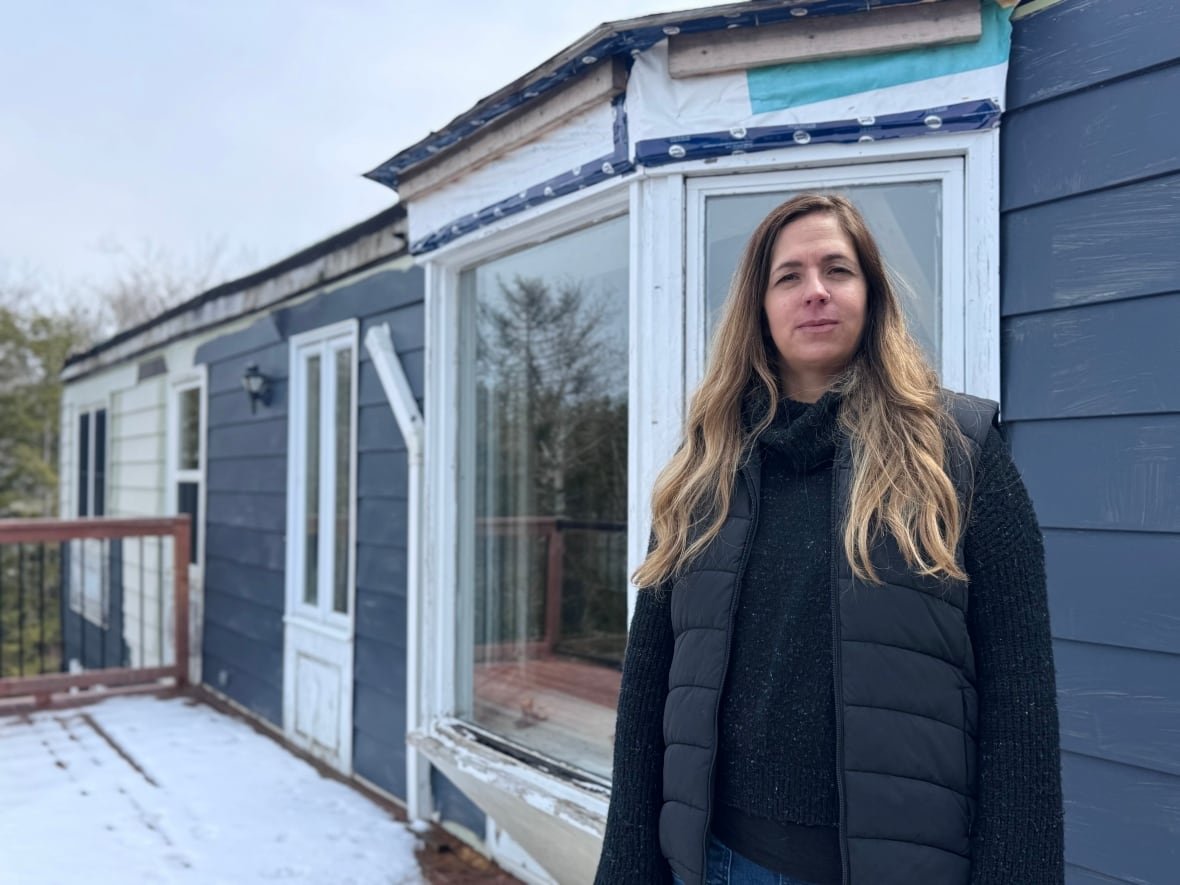 A woman stands outside of a home that has suffered storm damage.
