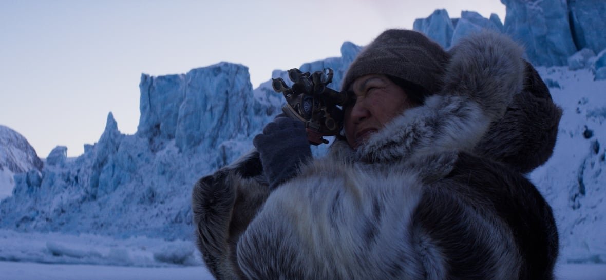 A woman in a fur jacket looks through a sextant. Behind her are ice pressure ridges. 