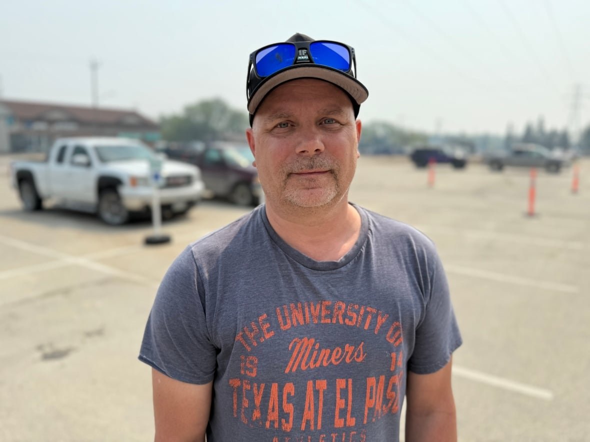 A man wearing a grey t-shirt and a hat looks at the camera. 