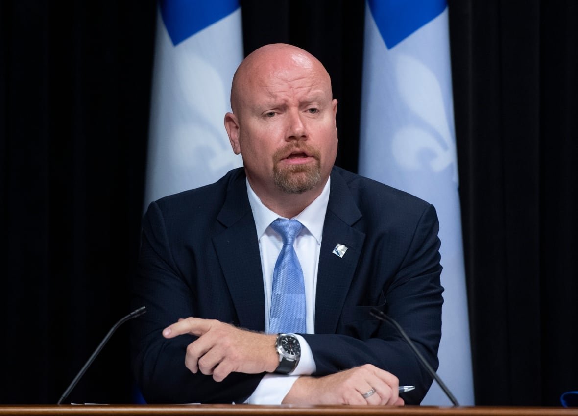 Ian Lafrenière speaking at a conference flanked by Quebec flags.