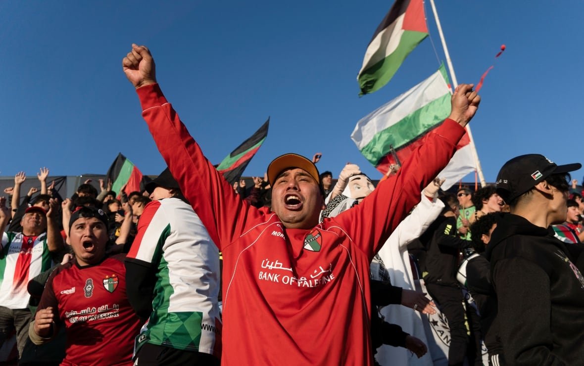 A man in a red Palestino shirt and cap celebrates a goal.