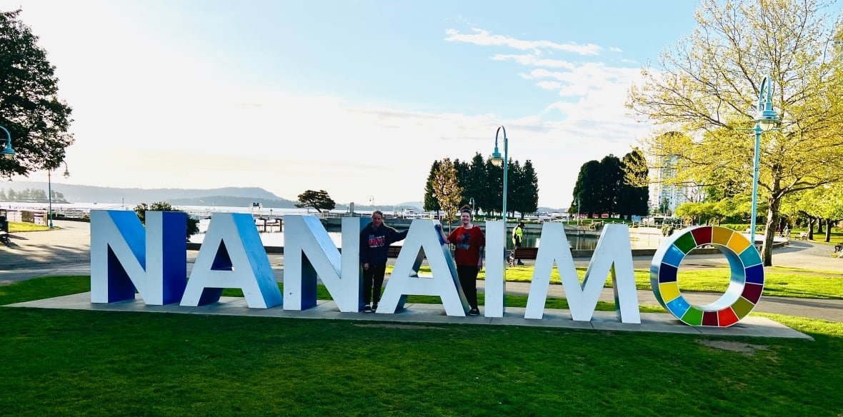 Two women stand smiling beside large block letters spelling Nanaimo in a waterfront park. 