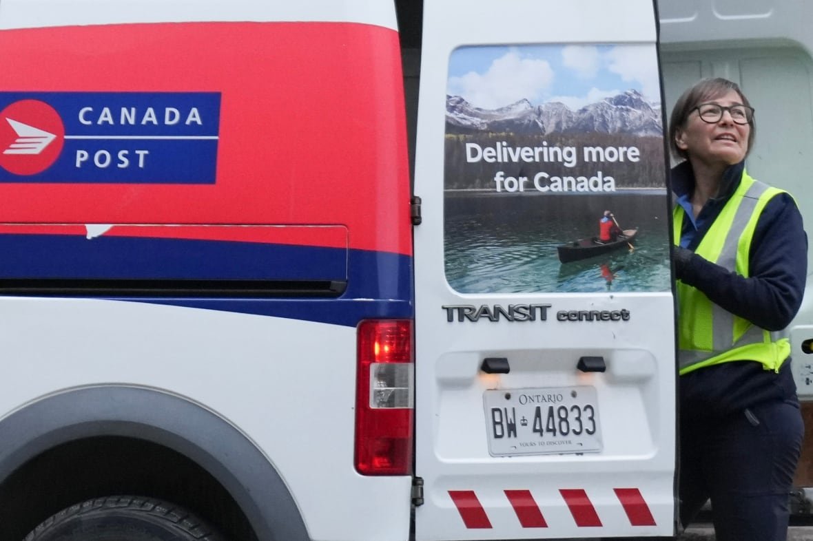 A Canada Post letter carrier stands at the back of a white van. 