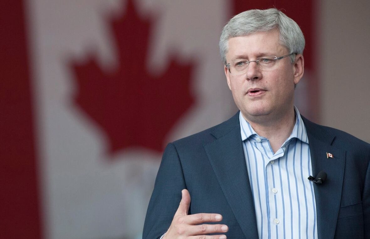 A man gestures while speaking, standing in front of a Canadian flag.