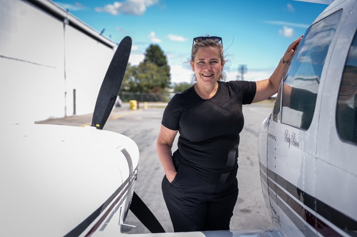 A woman wearing a black top and black pants poses next to an aircraft propeller.
