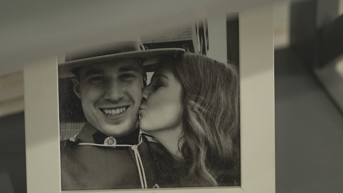 A woman with long hair kisses the cheek of a man in a Mountie hat.