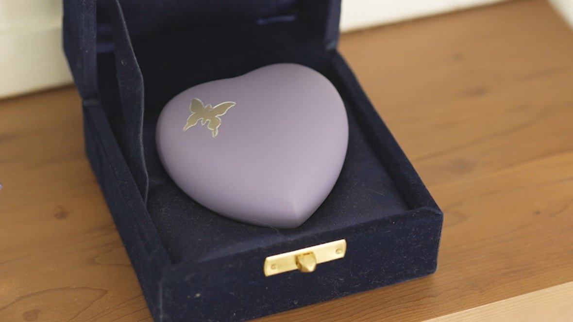 A heart-shaped purple urn with a gold butterfly sits on a mantle.