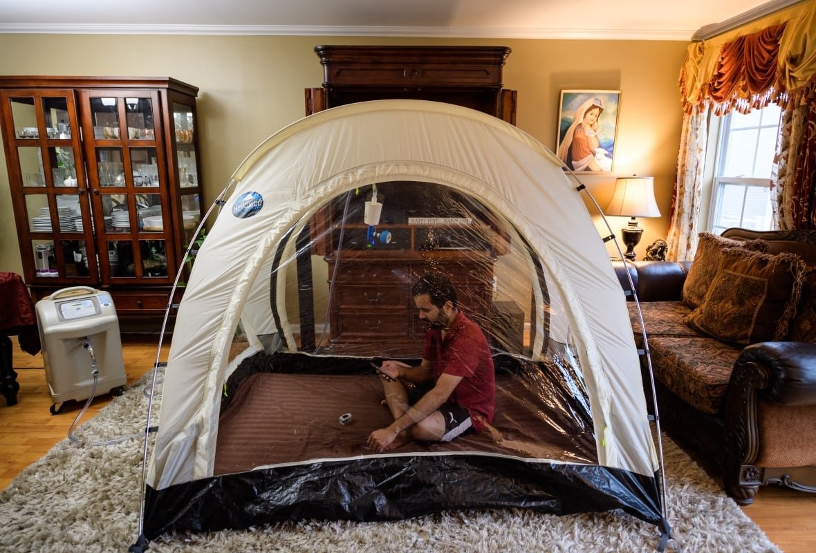 A man sits cross-legged in a tent set up in a living room. 