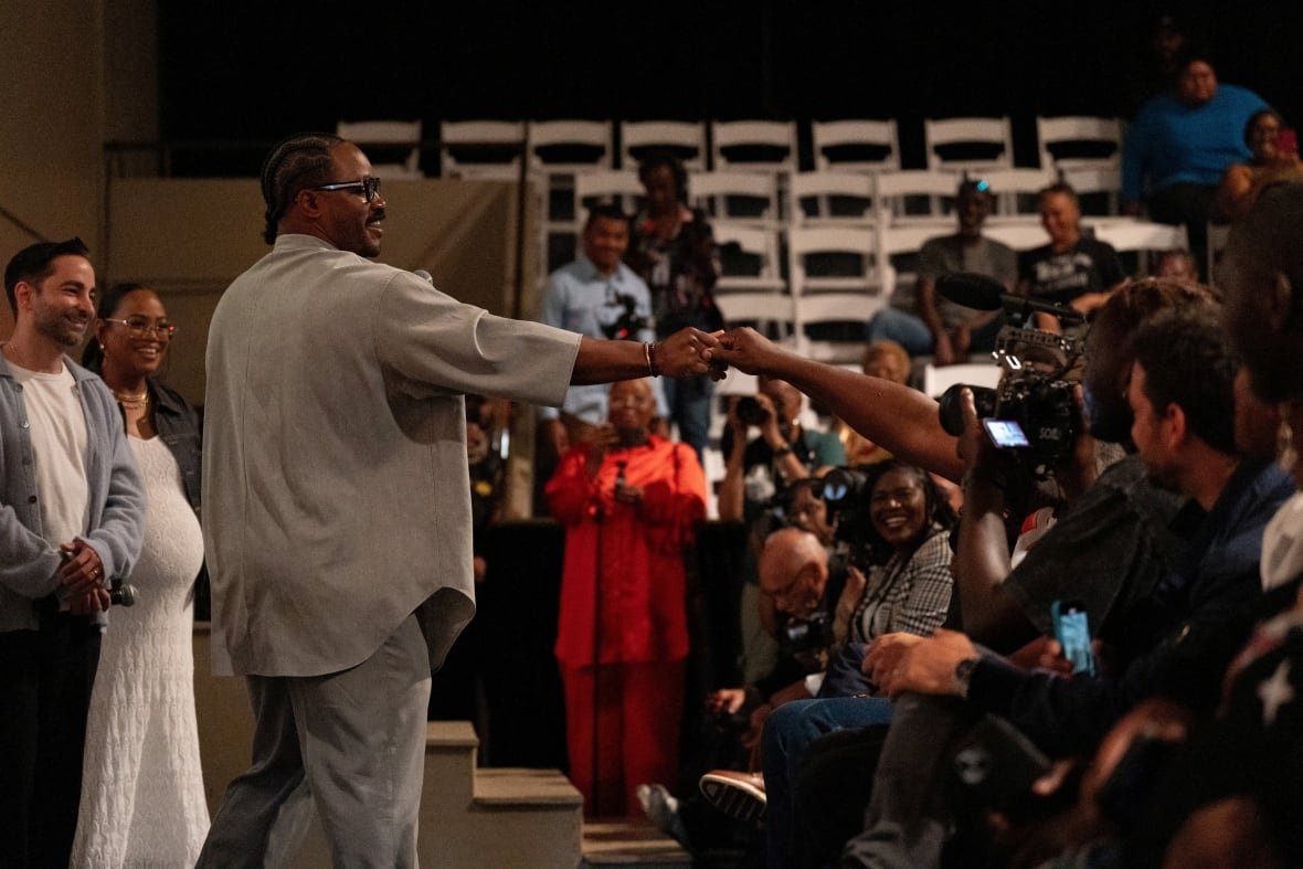 A man on stage fist-bumps an audience member in a crowded auditorium