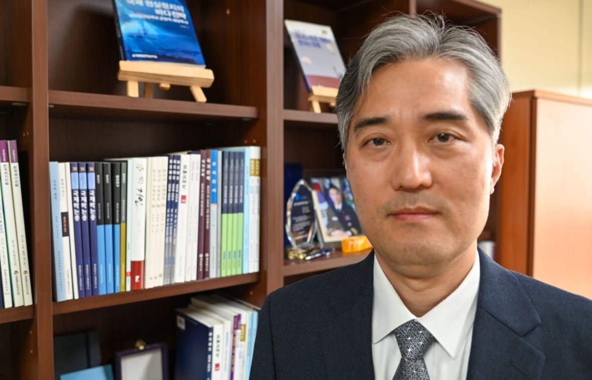 A man stands by a bookcase.