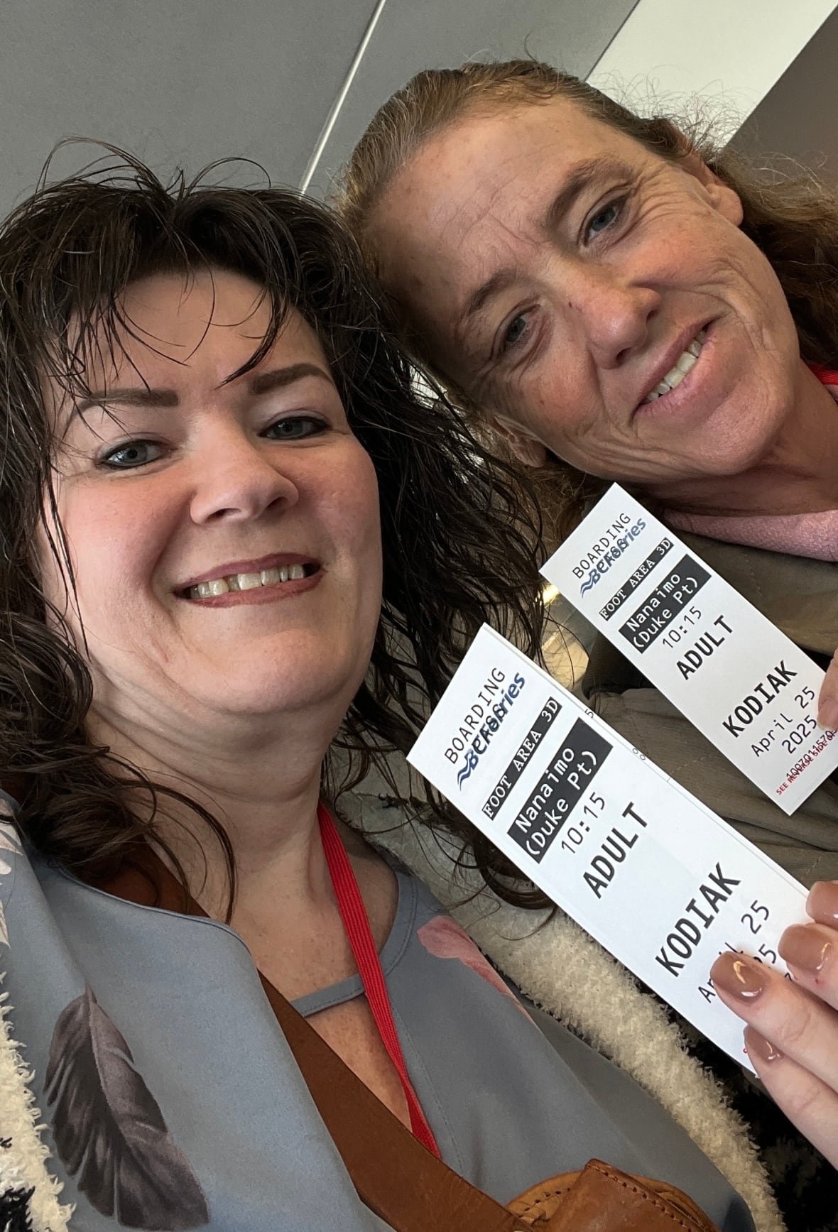 Two women photographed head-to-head show off their ferry boarding passes.