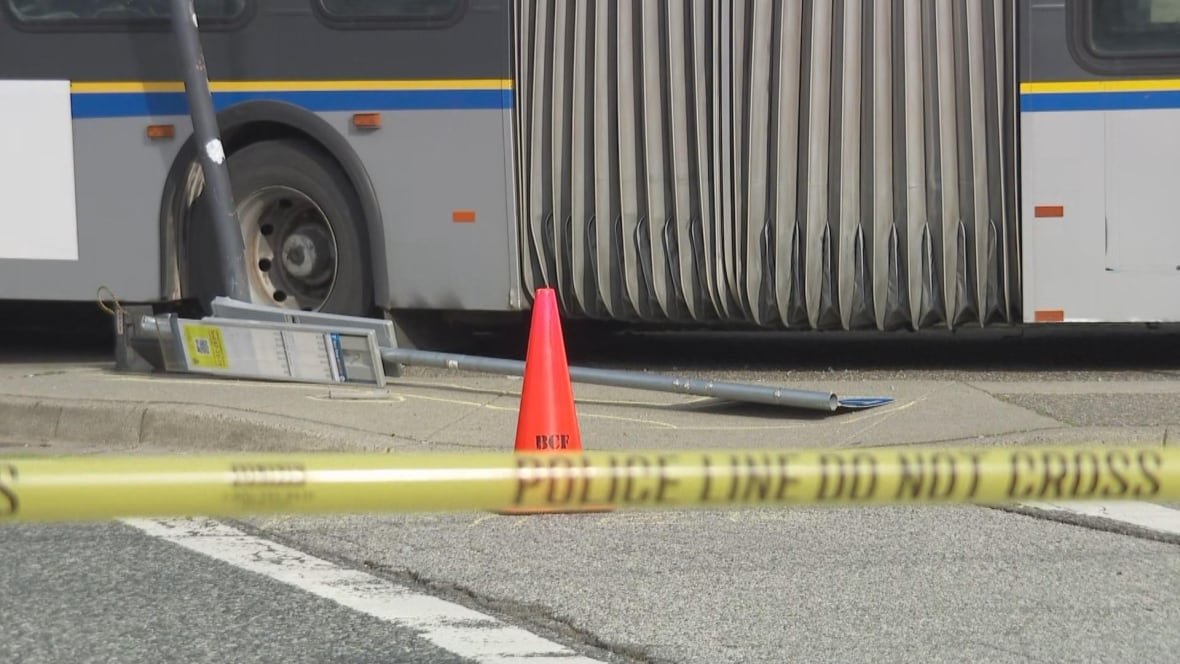 A bus beside a fallen bus stop sign in front of police tape and an orange cone.