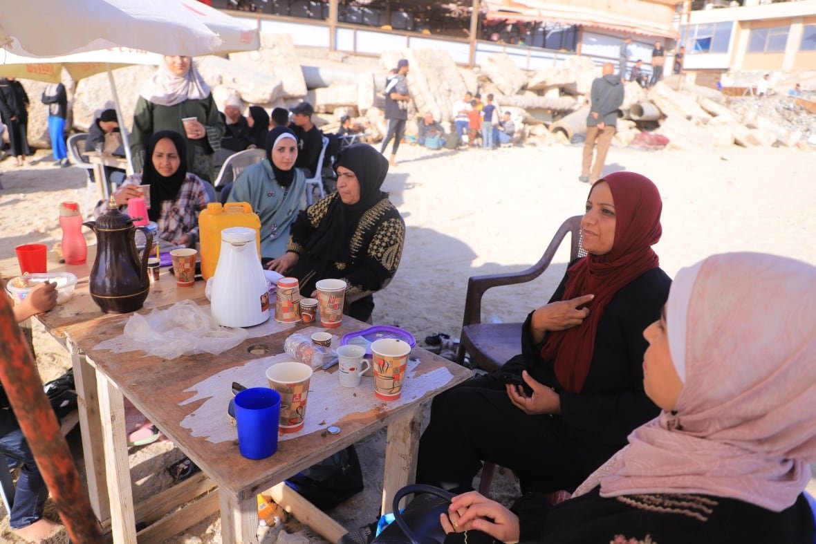 women wearing hijabs sit around a table at the beach
