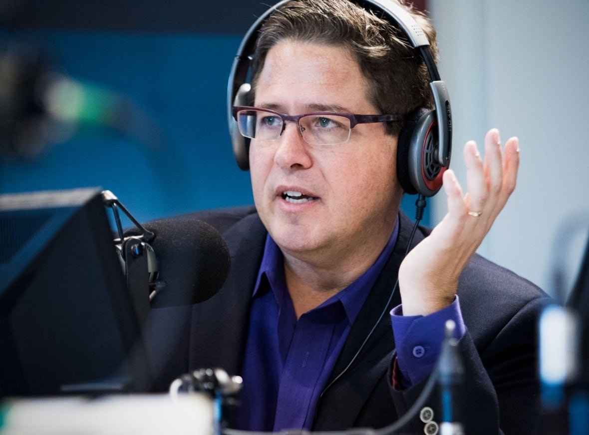 A broadcaster gestures while speaking into a microphone. 