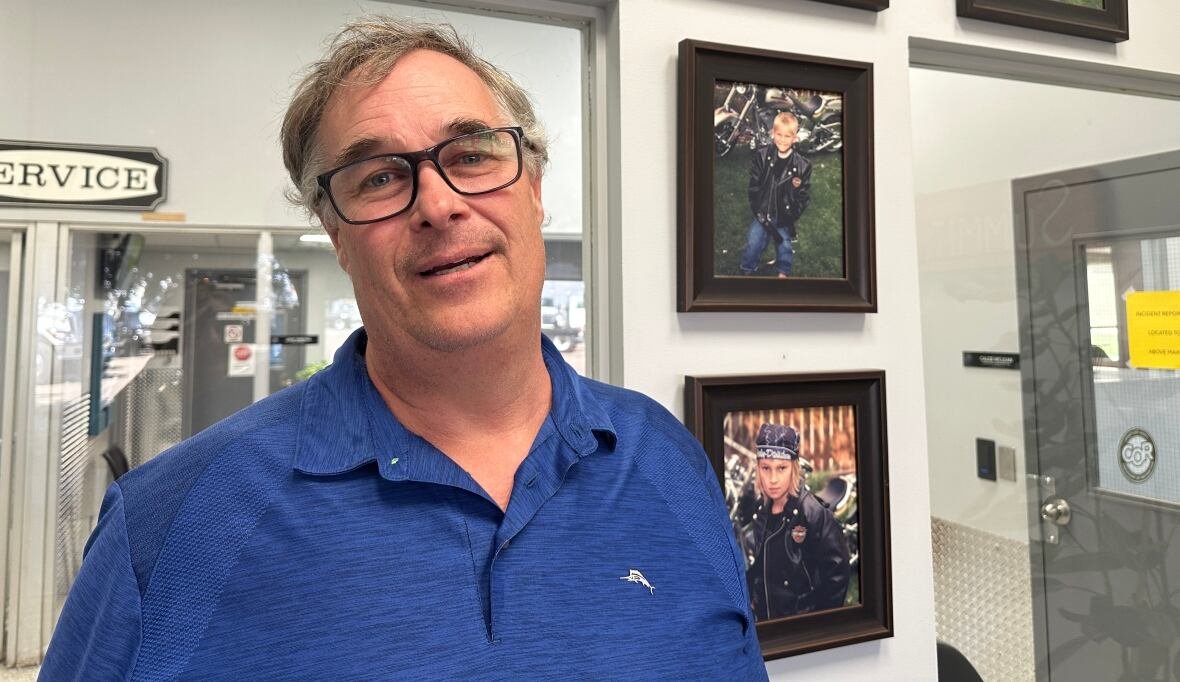 A man stands in front of photos of his family in an office. 