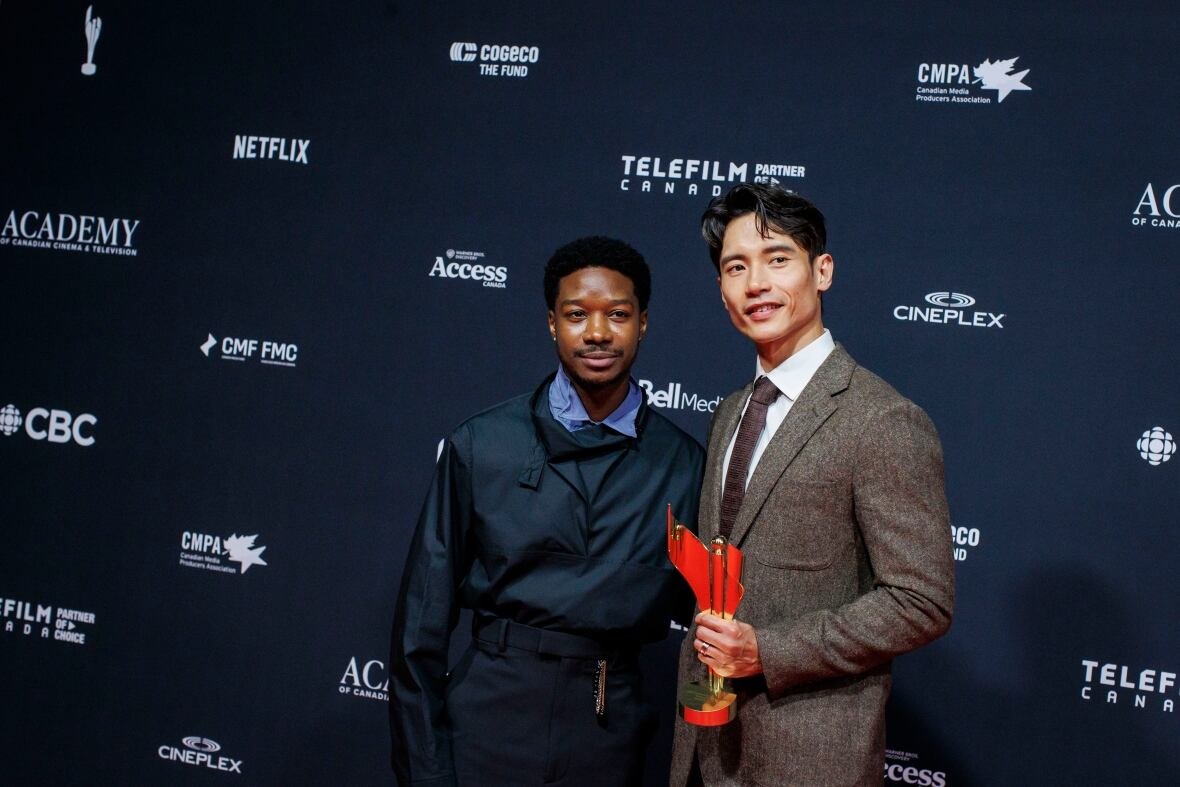 Two men wearing suits pose with a trophy.
