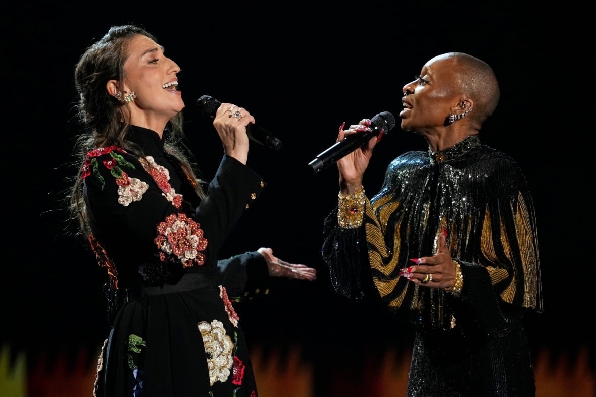Two women hold microphones and sing facing each other 