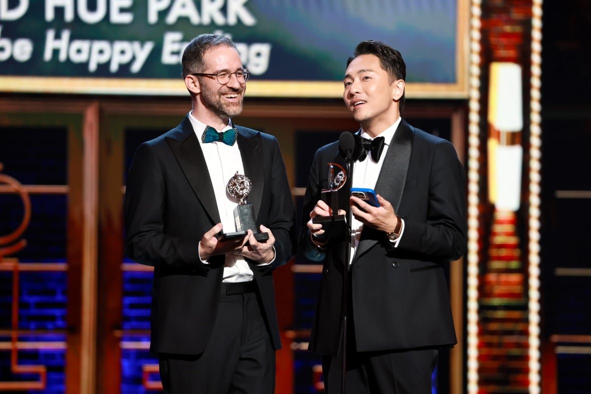 Two people hold their awards as they make an acceptance speech onstage.
